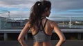 Fitness woman in grey sports crop with hands on hips and looking out from a rooftop