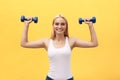 Fitness woman lifting weights smiling happy isolated on yellow background. Fit sporty Caucasian female fitness model. Royalty Free Stock Photo