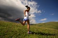 Fitness woman runner running on mountain grassland under dark clouds