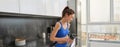 Fitness woman standing with black water bottle in kitchen, wearing workout clothing, drinking after yoga exercises Royalty Free Stock Photo