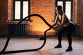 Fitness young athletic woman with strong beautiful body in black activewear exercising with battle ropes having workout Royalty Free Stock Photo