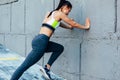 Rear view of fitness young woman doing stretching workout on a concrete grey wall. Athlete female exercising in morning outside Royalty Free Stock Photo