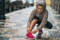 Fitness young woman tying shoelaces in rainy city Royalty Free Stock Photo