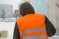 Fitter in a green jacket and orange vest, rear view