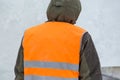 Fitter in a green jacket and orange vest, rear view