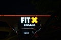 FitX glowing logo at night on building exterior, seen from parking lot with parked yellow sports car in front of it Royalty Free Stock Photo