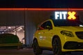 FitX glowing logo at night on building exterior, seen from parking lot with parked yellow sports car in front of it Royalty Free Stock Photo