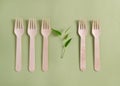 Five bamboo wood forks with a plant lie in a row on a green background. No plastic concept.