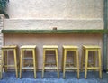 Five bar stools standing against a hard grained wall