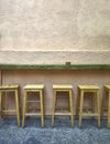 Five bar stools standing against a hard grained wall