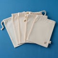 Five beige drawstring fabric bags are displayed on a blue textured surface Royalty Free Stock Photo