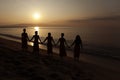 Five black women hold hands looking at the sunrise at the beach.