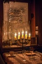 Five candles burning in menorah on a table on foreground and frosted window with snowed tree outside