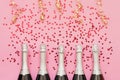 Five Champagne bottles with confetti stars and party streamers on pink background. Copy space,top view. Party background Royalty Free Stock Photo