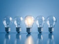 Five classic light bulbs lined up in a row with the middle bulb illuminated symbolizing creativity, innovation, and standing out Royalty Free Stock Photo