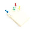 Five color push pins and yellow sticky note on isolated white ba