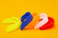 Five colored boxing mouth guards laid out in a row on a yellow background, concept