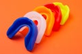 Five colored boxing mouth guards, lying side by side, on an orange background