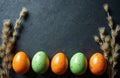 Five colored quail eggs, orange and green, sit in a row with fluffy willow branches. The festive Easter composition has a dark Royalty Free Stock Photo