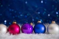 Five colorful Christmas balls on white fur with garland lights o Royalty Free Stock Photo