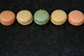 Five colourful macaroons in a row are on the black background. Five tasty cookies