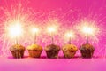 Five Cupcakes with a sparkler over a pink background.