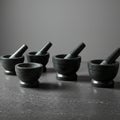 Five dark-colored mortar and pestle sets are arranged on a textured dark surface. Th Royalty Free Stock Photo