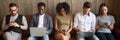 Five diverse businesspeople girls guys sitting on couch using gadgets