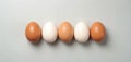 Five eggs are in row. Two white eggs and three brown eggs. One brown egg is speckled. They sit on light gray surface. Minimalist, Royalty Free Stock Photo