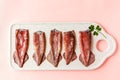 Five fresh ancooked squids with leaf of parsley on white plate on pink background. Top view Royalty Free Stock Photo