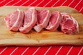 Five fresh raw lamb loin chops on a wooden cutting board and traditional butcher red and white stripe apron Royalty Free Stock Photo
