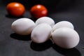 Five fresh white eggs and tomatoes on black surface Royalty Free Stock Photo