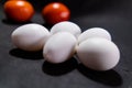 Five fresh white eggs and tomatoes on black surface Royalty Free Stock Photo