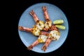 Five grilled shrimps with cheese on blue plate isolated on black background top view