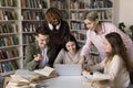 Five happy multiracial groupmates discuss online task use laptop