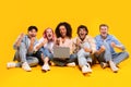 Five international students sitting with laptop and shaking fists in joy, reading great news over yellow background