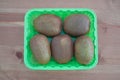 Five Kiwi fruits in a green box on wooden background