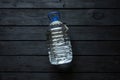 A five-liter plastic water bottle lies on a black wooden board