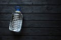 A five-liter plastic water bottle lies on a black wooden board