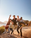 Five millennial friends on a road trip have fun posing for photos on a coastal path, full length