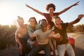 Five millennial friends on a road trip have fun posing for photos at the roadside, close up