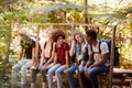 Five millennial friends sitting on a bridge in a forest talking during a hike, three quarter length