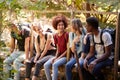 Five millennial friends sitting on a bridge in a forest talking during a hike, three quarter length