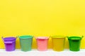 Five multi-colored buckets on a yellow background with place for text, yellow, pink, red, green, turquoise buckets, gardening