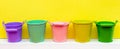 Five multi-colored buckets on a yellow background with place for text, yellow, pink, red, green, turquoise buckets, gardening