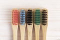 Five multicolored bamboo toothbrushes on white wooden table.