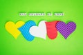 Five multicolored valentine hearts and the inscription All Colours of Love made of white alfphabet cubes on a green background