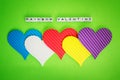 Five multicolored valentine hearts and the inscription Rainbow Valentine made of white alfphabet cubeson a green background
