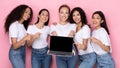Five multiracial ladies showing laptop with empty screen, pink background