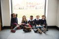 Five primary school friends with tablet computers sitting on the floor in a school corridor at break time, smiling to camera, sele